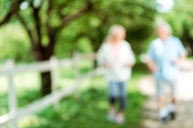 blurred view of retired woman running near senior man in park  clipart
