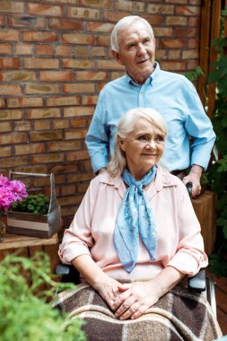 selective focus of senior man standing near cheerful disabled wife clipart