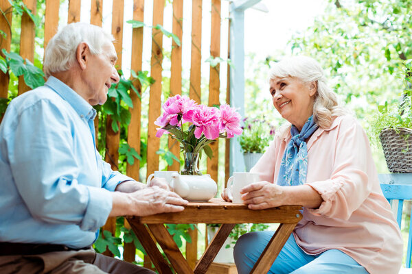 Низкий угол обзора счастливого пожилого мужчины, смотрящего на веселую жену возле розовых цветов
 