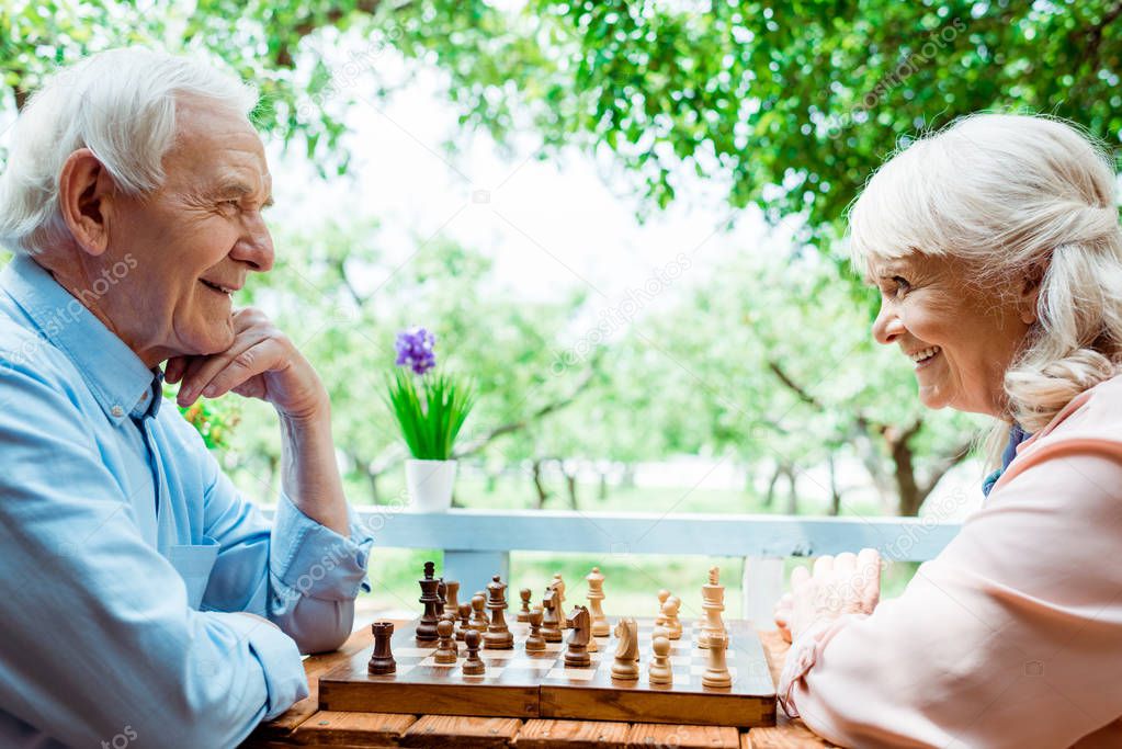 cheerful retired woman with grey hair playing chess with senior husband 