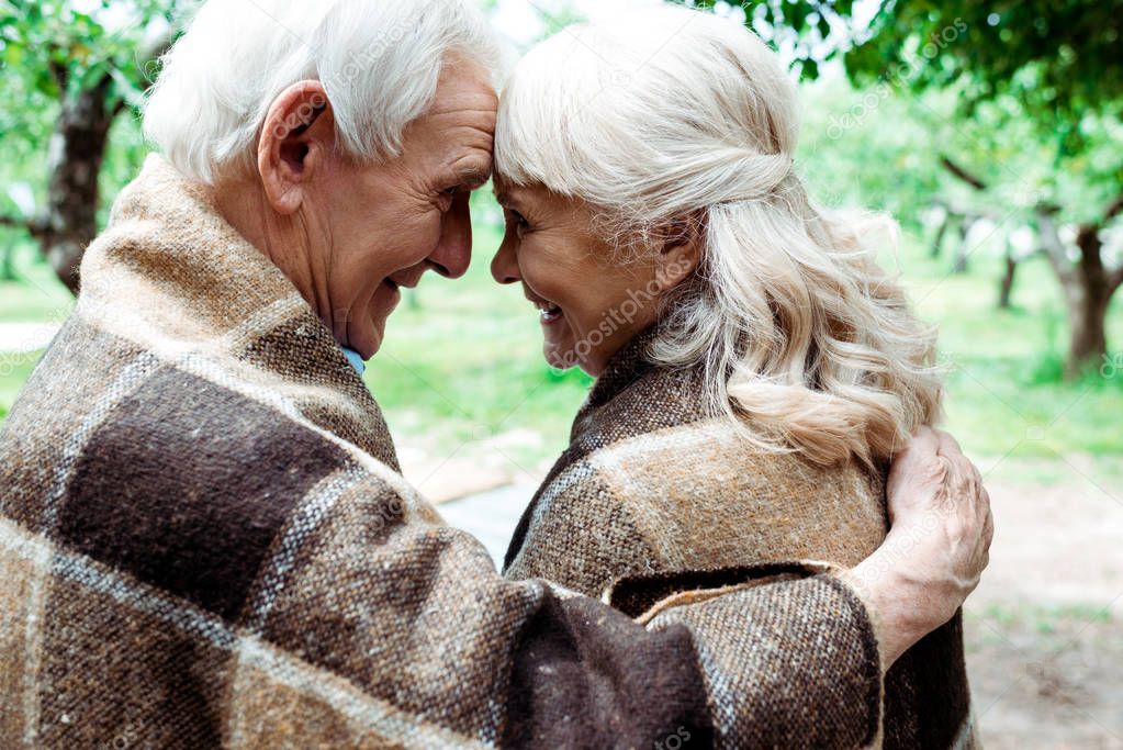 happy senior woman and man in blankets looking at each other 