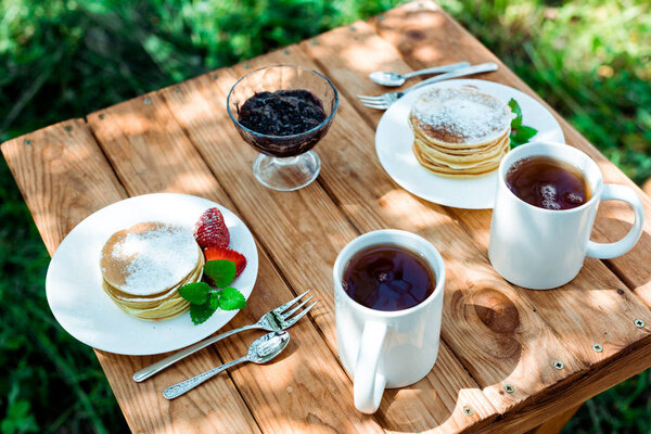 overhead view of tasty pancakes with organic strawberries near cups with tea 