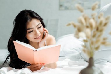 evde yatakta yatarken olumlu asyalı kız okuma kitap seçici odak 