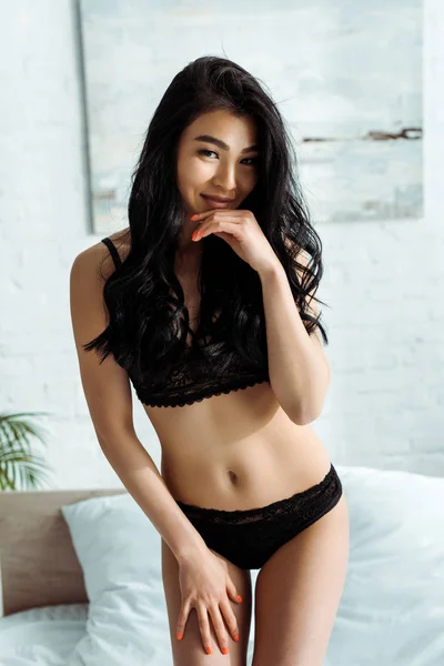 顔に触れながら微笑む黒い下着を着た陽気なアジア人女性 — ストック写真