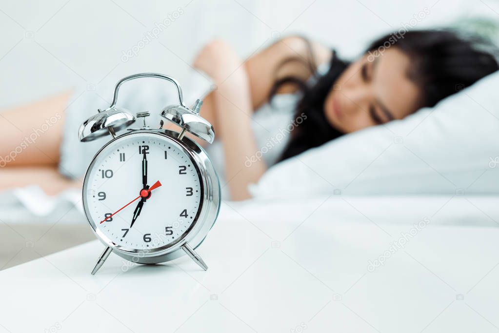 selective focus of retro alarm clock near sleeping girl 