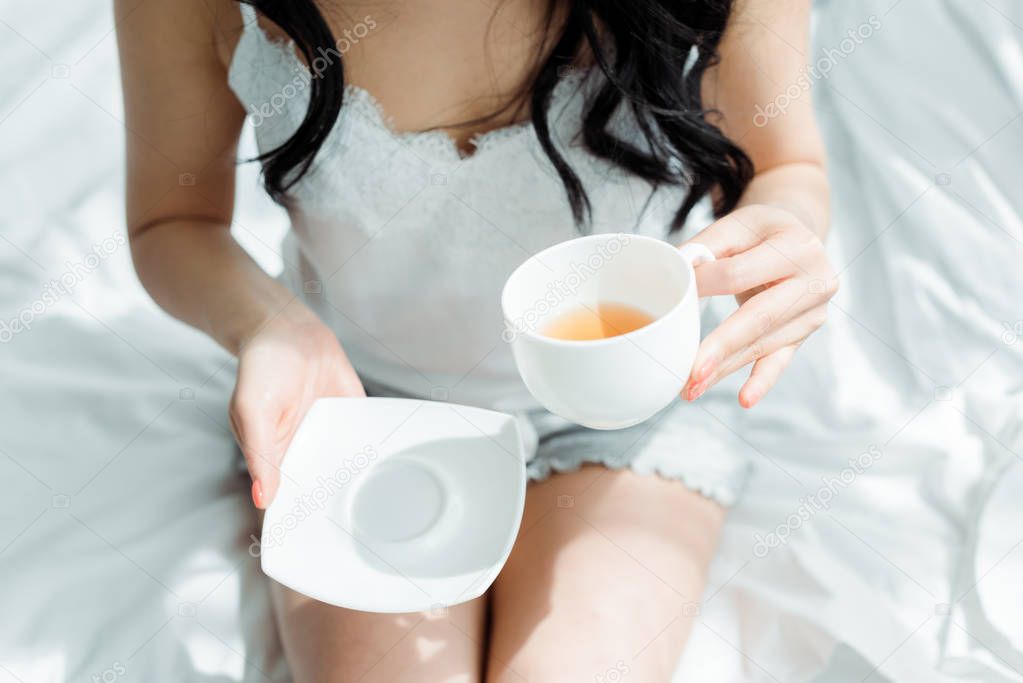 overhead view of brunette woman holding cup with tea in bedroom 