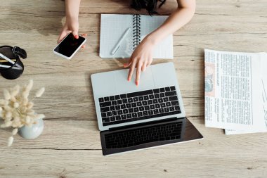 boş ekranlı dizüstü bilgisayar ve akıllı telefon kullanan genç kadının kırpılmış görünümü