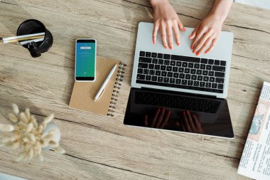 Kiev, Ukrayna - 23 Mayıs 2019: twitter uygulaması ile akıllı telefon yakınında boş ekran ile dizüstü bilgisayar kullanarak genç kadın kırpılmış görünümü