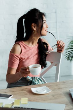 dudakları ve çay fincan yakınında gazlar tutan mutlu genç asya kadın seçici odak 