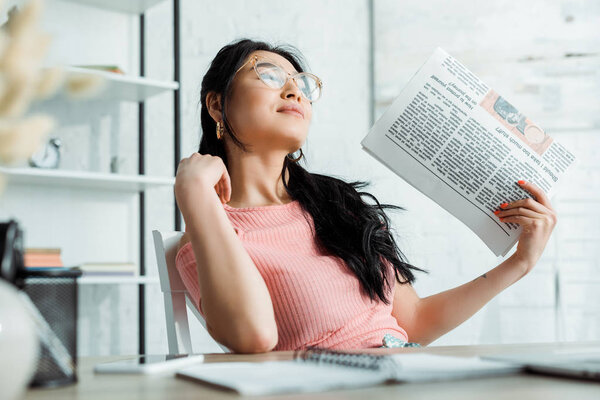 селективный фокус привлекательной тайки в очках с газетой
 