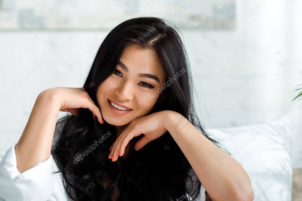 cheerful thai woman smiling at touching face while looking at camera 