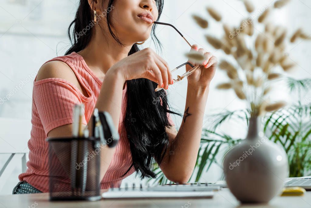 selective focus of woman holding gasses near pen holder in office 