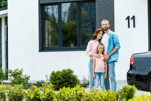 Wesoły Człowiek Stojący Atrakcyjną Żoną Uroczym Dzieckiem Pobliżu Nowego Domu — Zdjęcie stockowe