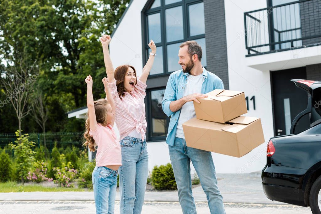 happy woman and kid gesturing near bearded man with boxes