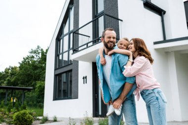 happy bearded man piggybacking daughter near cheerful wife and home  clipart