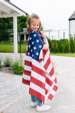 evin yakınında Amerikan bayrağı ile ayakta neşeli çocuk gülümseyen 