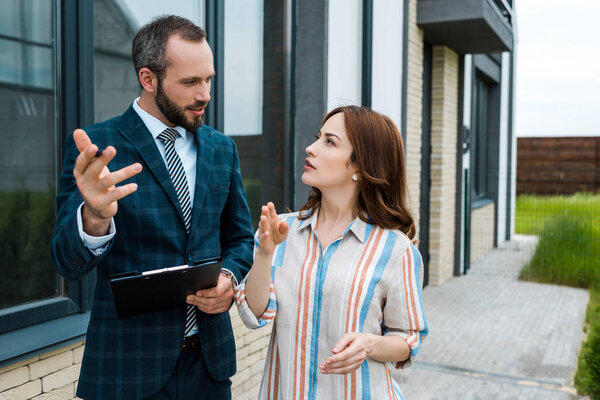 handsome bearded broker holding clipboard and gesturing near woman 