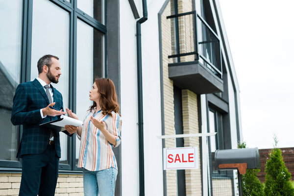 low angle view of woman gesturing while looking at broker near house 