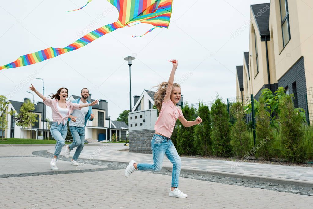 cheerful kid running with colorful kite near happy parents on street 