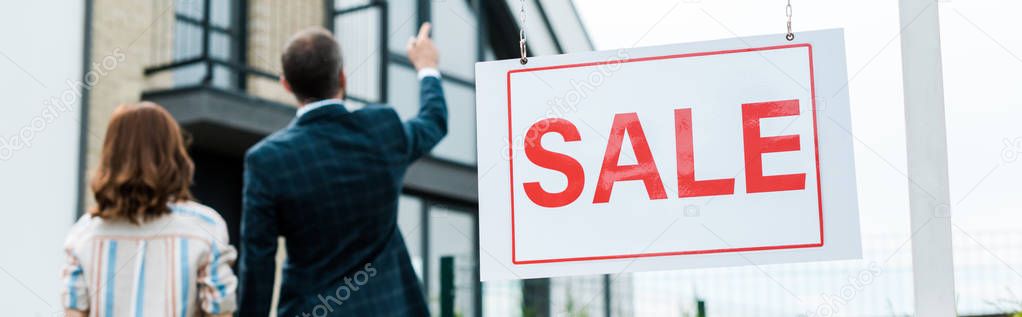 panoramic shot of broker pointing with finger at house while standing near woman 