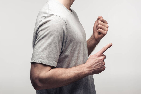 partial view of man holding fist and pointing with finger isolated on grey, human emotion and expression concept