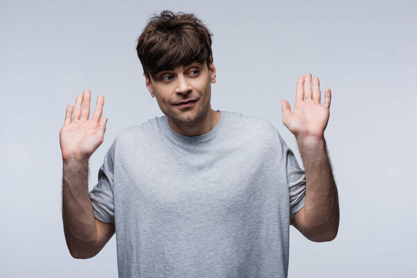 smiling man showing give up gesture and looking away isolated on grey, human emotion and expression concept