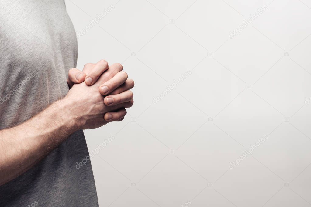 partial view of man holding clenched hands isolated on grey, human emotion and expression concept