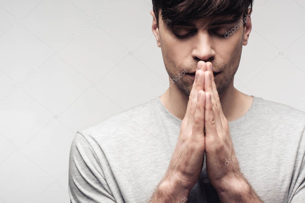 serious man with closed eyes showing praying gesture isolated on grey, human emotion and expression concept
