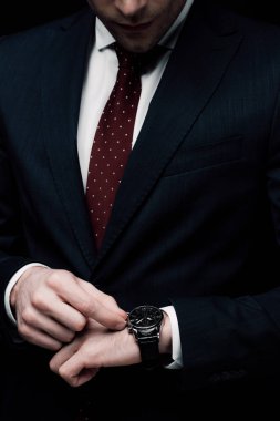 cropped view of businessman checking time on watch isolated on black clipart