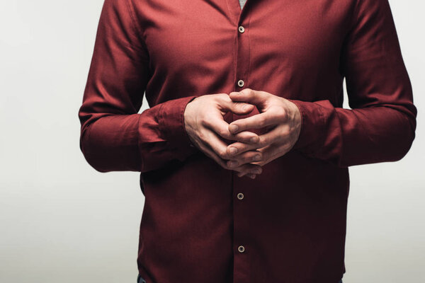 partial view of man standing with clenched hands isolated on grey, human emotion and expression concept