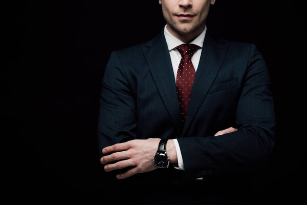 partial view of businessman standing with crossed arms isolated on black