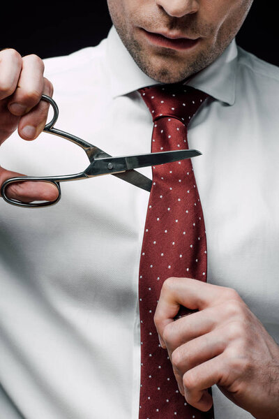 cropped view of displeased businessman cutting tie with scissors isolated on black