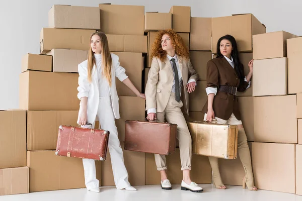 Multicultural girls standing with suitcases near boxes on white — Stock Photo, Image