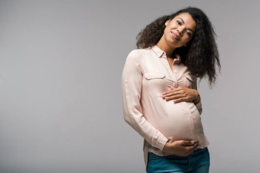 gri ayakta iken karnına dokunan gülümseyen genç hamile afrikalı amerikalı kadın 