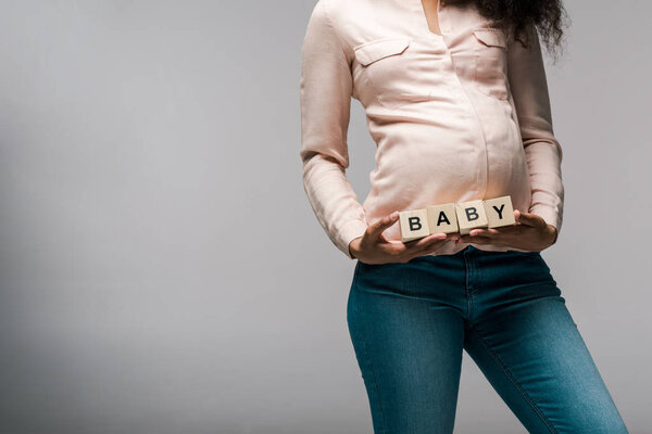 cropped view of african american girl holding wooden cubes with baby letters on grey 
