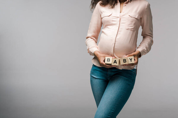 cropped view of african american woman holding wooden cubes with baby letters on grey 