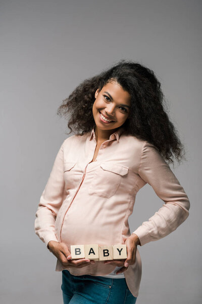 happy african american girl holding wooden cubes with baby letters on grey 