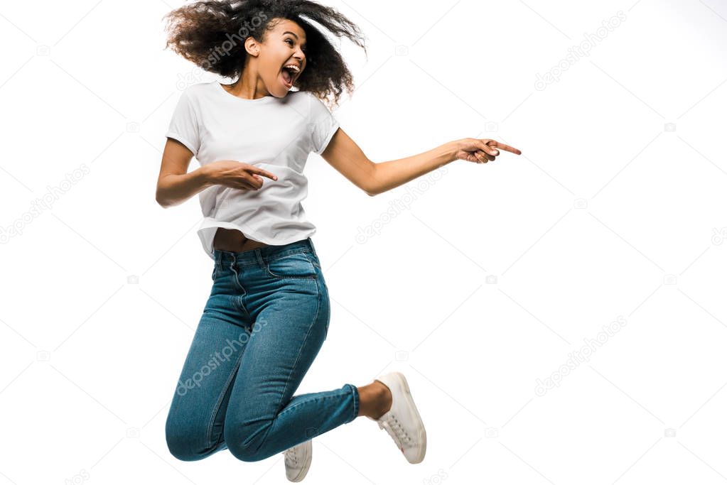 cheerful african american woman pointing with fingers and jumping isolated on white 
