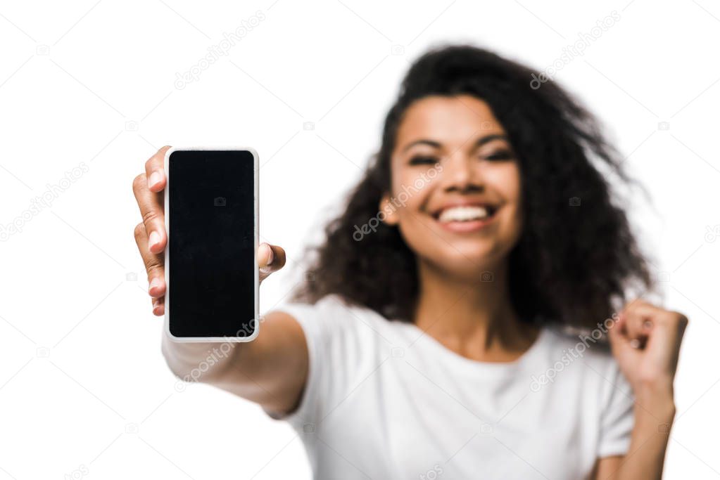 selective focus of positive african american girl holding smartphone with blank screen and celebrating isolated on white 