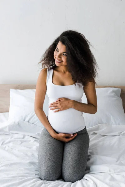 Yatakta Otururken Karnına Dokunan Pozitif Kıvırcık Afrikalı Amerikalı Hamile Kadın — Stok fotoğraf