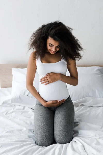 Encaracolado Africano Americano Mulher Grávida Tocando Barriga Enquanto Sentado Cama — Fotografia de Stock