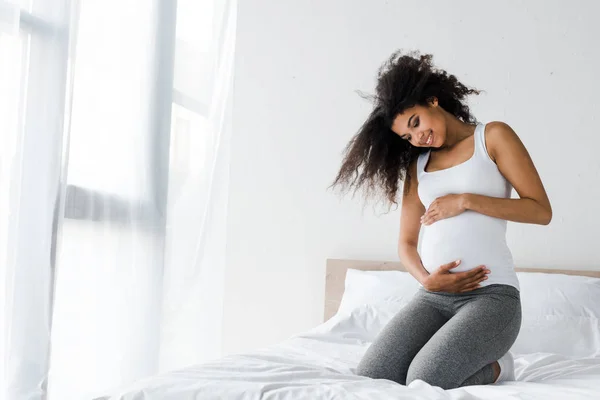 Feliz Embarazada Africana Americana Mujer Tocando Vientre Mientras Sentado Cama —  Fotos de Stock