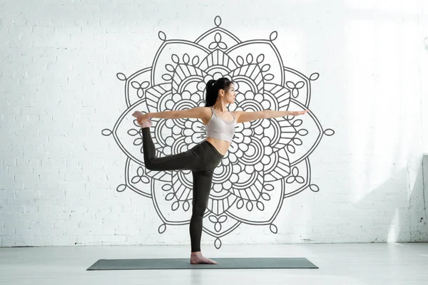 asian woman practicing yoga on yoga mat near mandala ornament