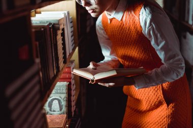 kütüphanede kitap tutan turuncu elbiseli kadının kırpılmış görünümü 