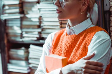 kütüphanede turuncu kitap tutan gözlük kadın kırpılmış görünümü 