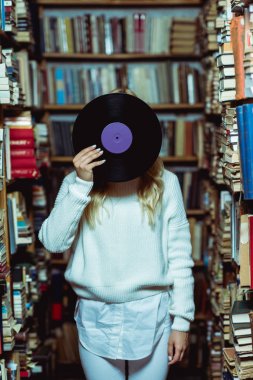  young adult woman in white sweater holding vinyl in library  clipart