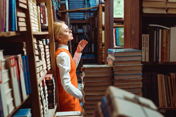 漂亮和金发女人在橙色礼服和眼镜站在图书馆 — 图库照片