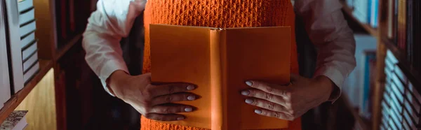 在图书馆中拿着橙色书籍并带有复制空间的妇女的裁剪视图 — 图库照片