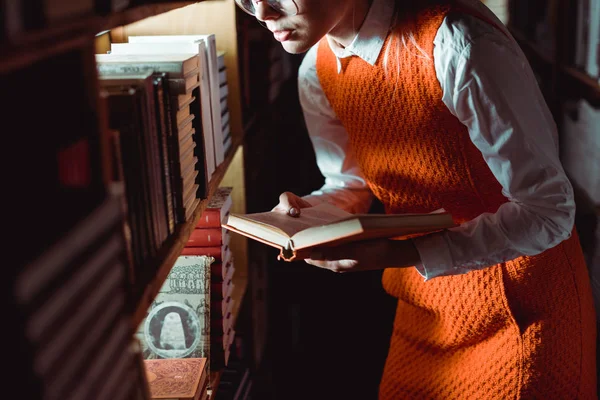 Περικομμένη Θέα Της Γυναίκας Πορτοκαλί Φόρεμα Κρατώντας Βιβλίο Στη Βιβλιοθήκη — Φωτογραφία Αρχείου