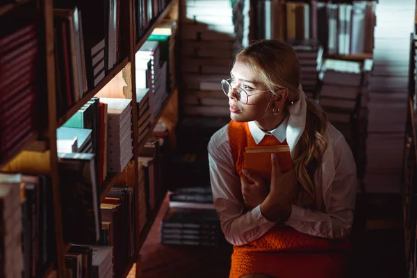 Mulher Assustada Bonita Óculos Segurando Livro Olhando Para Longe Biblioteca — Fotografia de Stock